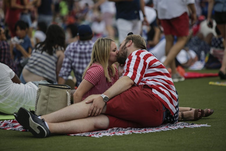A couple kissing, sitting outside in a park.